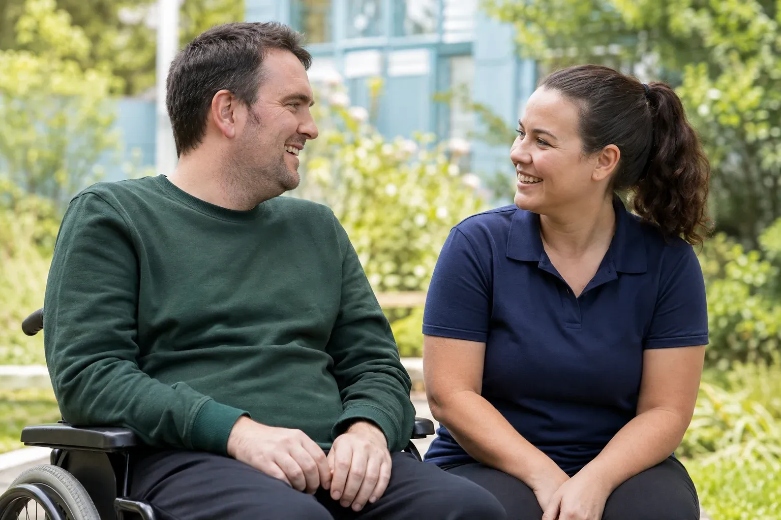 A wheelchair user and a support worker sharing a smile in a sunlit garden
